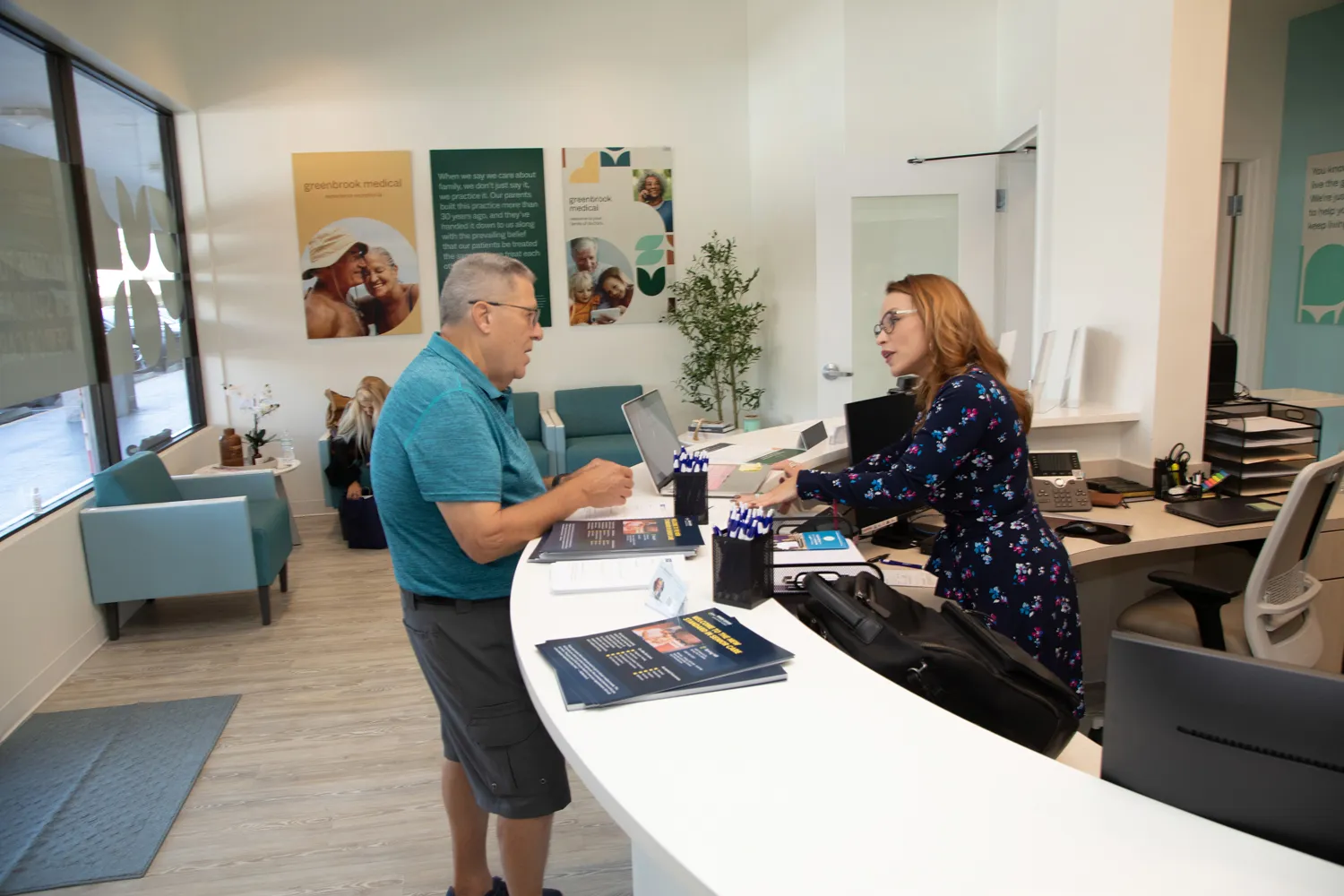 Senior patient checking in at the Greenbrook Medical front desk with a friendly staff member in a welcoming clinic waiting area